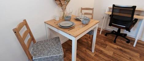 Een eetgedeelte met een houten tafel, twee stoelen, een vaas met bloemen en een zwarte bureaustoel.