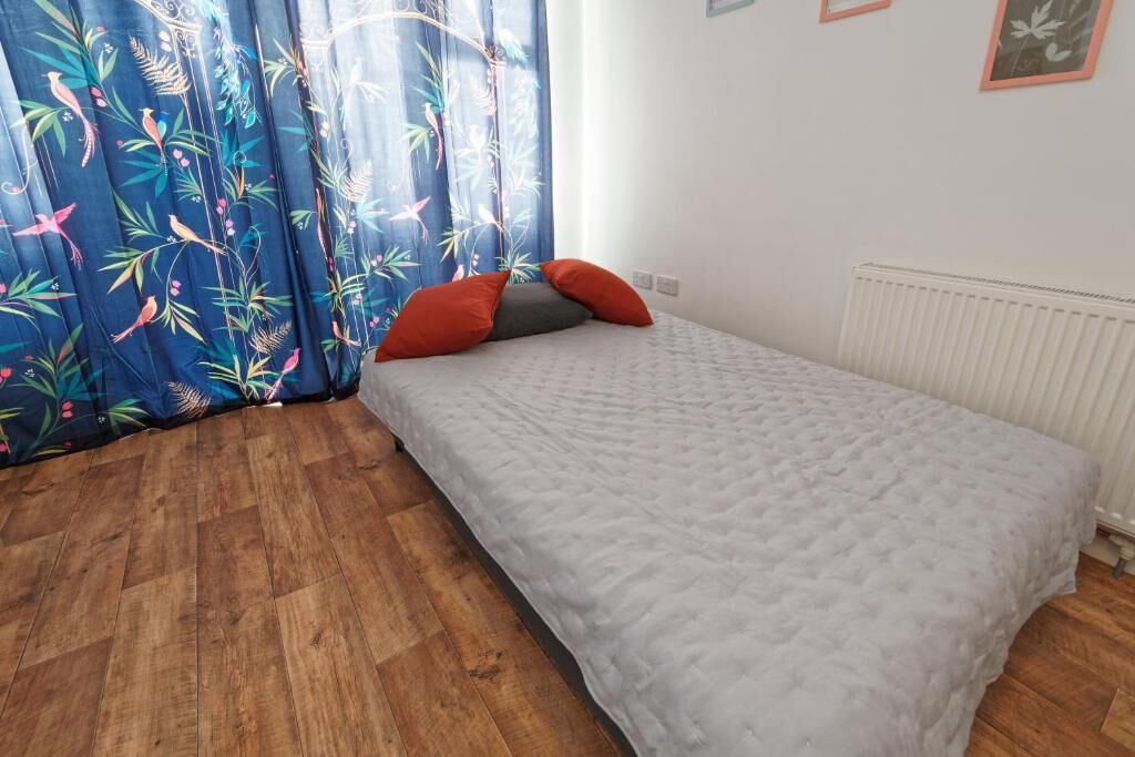 Un dormitorio con cama, suelo de madera y ventana con cortinas.