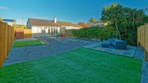 A residential backyard with a lawn, a patio area with seating, and a wooden fence.