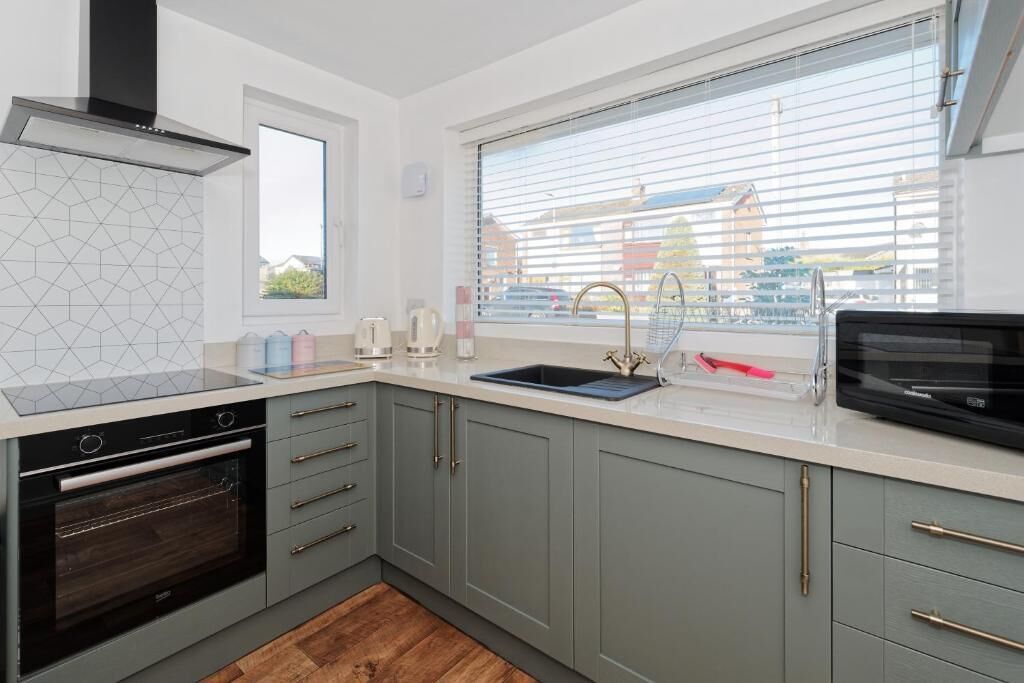 A modern kitchen with a built-in oven, a sink, and a window with blinds.
