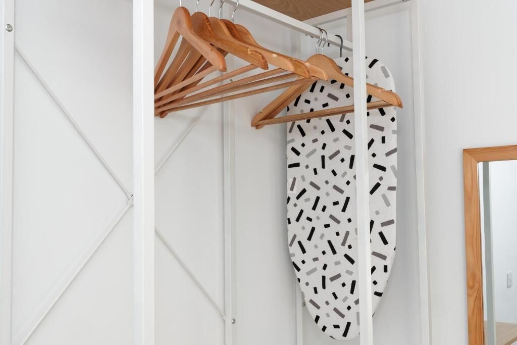 Una habitación blanca con un perchero de madera y una cortina de ducha estampada.