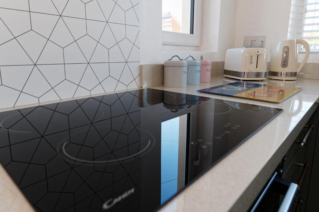 Een moderne keuken met een zwart inductiekookveld, een broodrooster, een waterkoker en kleurrijke opbergboxen.