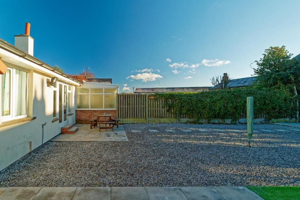 A residential backyard with a patio, a wooden fence, and a gravel area.