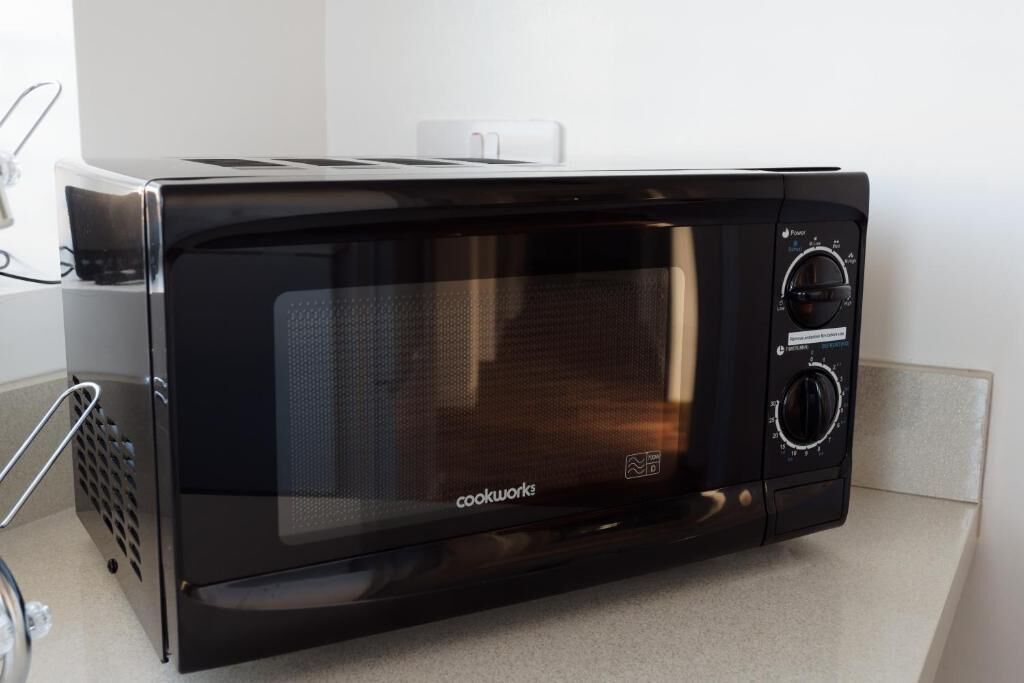 Eine schwarze CookWorks-Mikrowelle mit digitaler Anzeige und Bedienfeld steht auf einer Küchenarbeitsplatte.