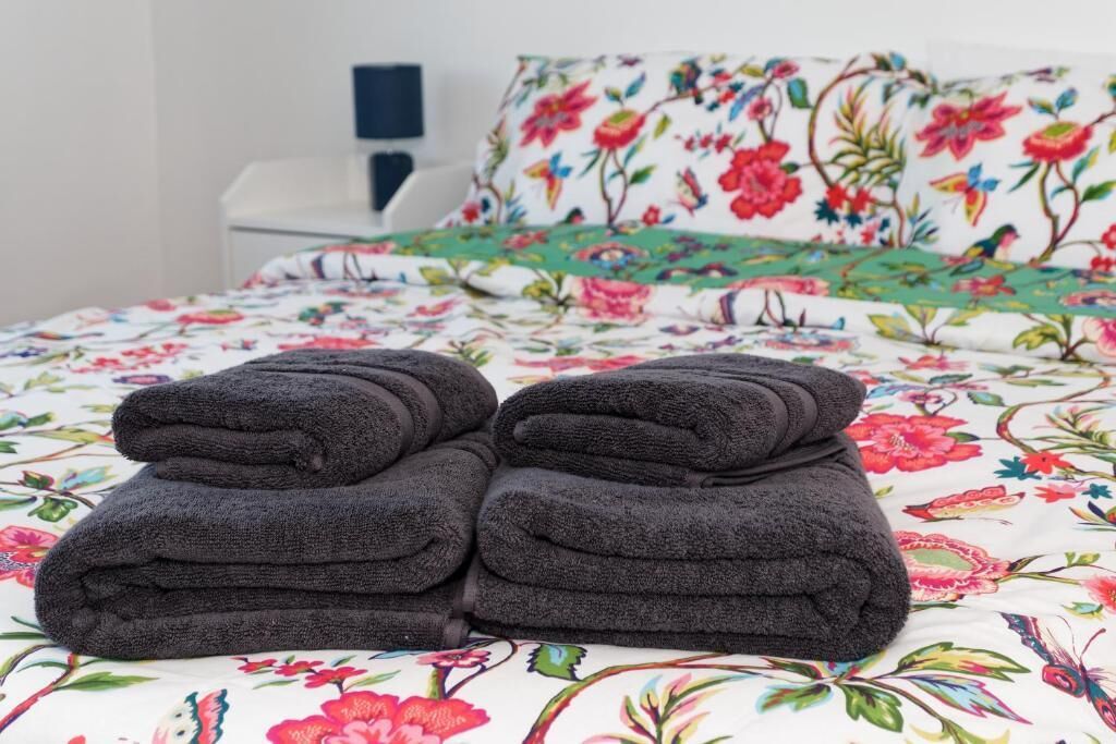 Un letto con una coperta a fiori e due asciugamani piegati di colore scuro.