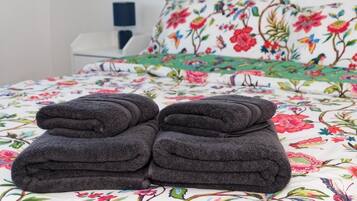 Un letto con una coperta a fiori e due asciugamani piegati di colore scuro.