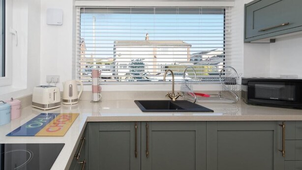 A modern kitchen with a built-in stove, a sink with a faucet, a microwave, and a window with blinds.