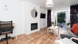 A modern living room with a fireplace, a round mirror, a television, and a dining area with a table and chairs.