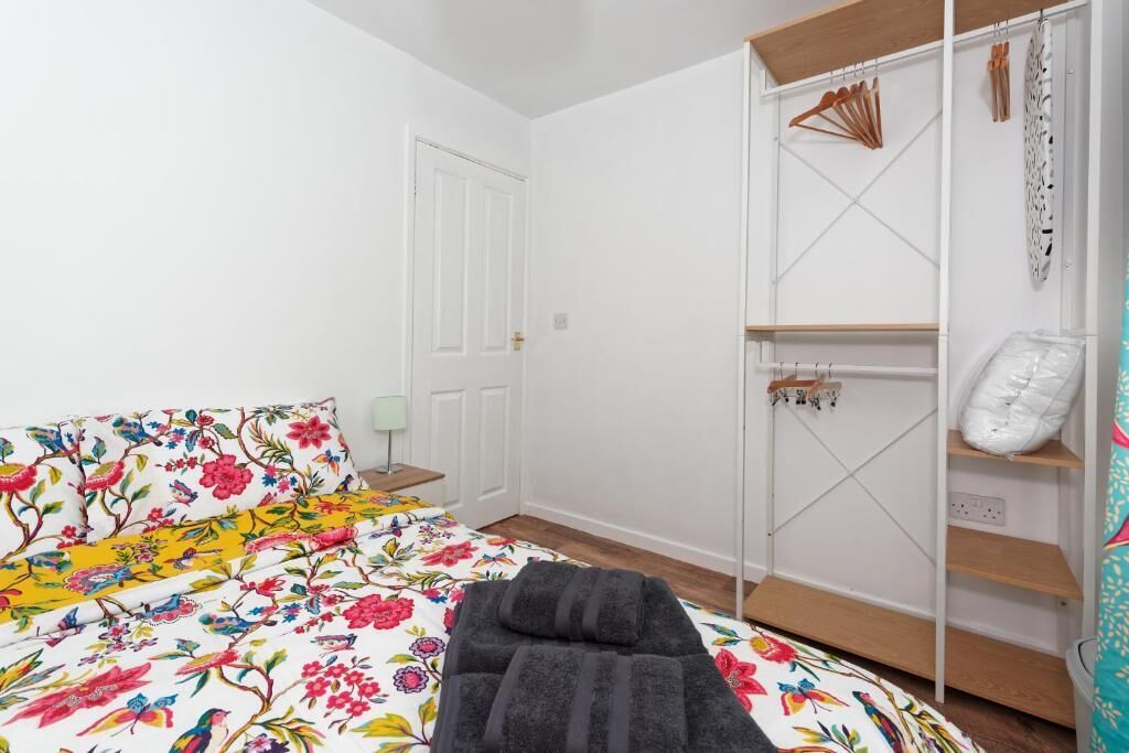 A bedroom with a floral bedspread, a grey rug, a white wardrobe with hanging space, and a wooden floor.