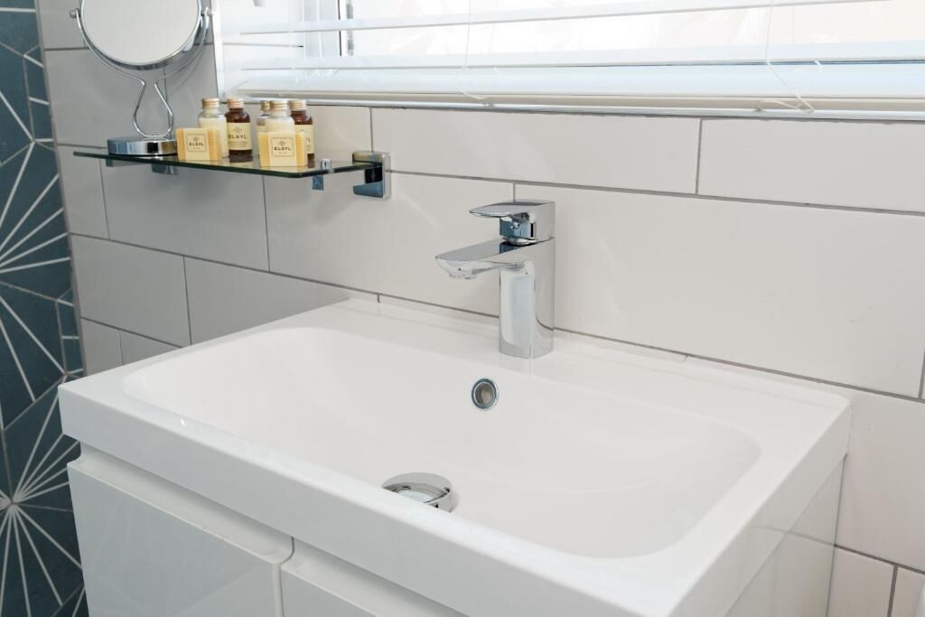 Une salle de bain moderne avec un lavabo blanc, un robinet chromé et une étagère contenant des articles de toilette.