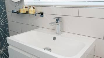 Une salle de bain moderne avec un lavabo blanc, un robinet chromé et une étagère contenant des articles de toilette.