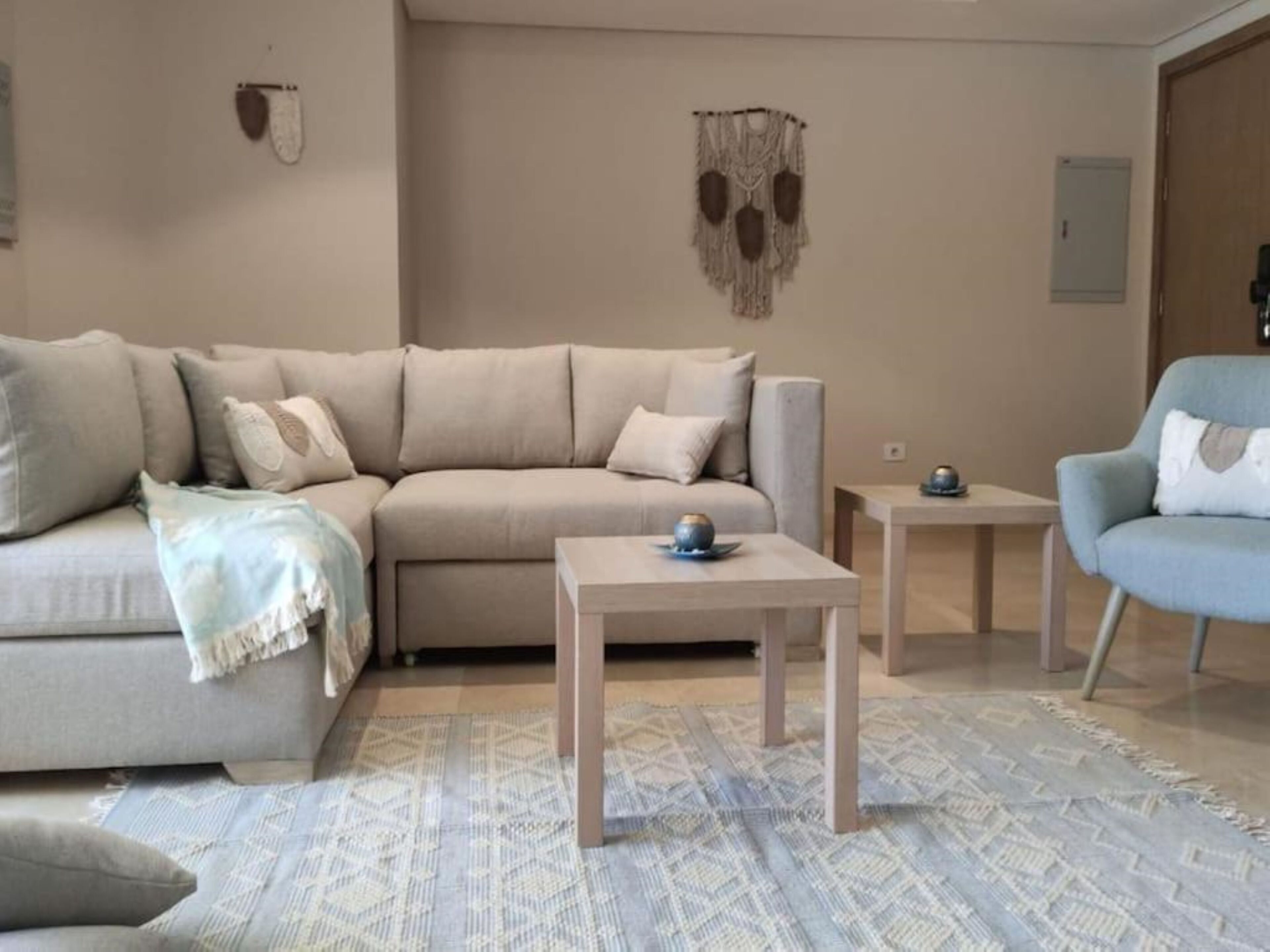 A living room with a beige sofa, a blue armchair, a small wooden table, and a patterned rug.