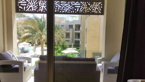 Un balcón con muebles de mimbre, una piscina y vistas a un edificio de varios pisos y balcones.
