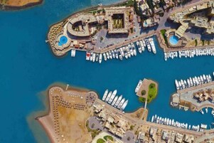 Vista aérea de un puerto deportivo con numerosas embarcaciones amarradas, un edificio central con piscina y zonas ajardinadas alrededor.