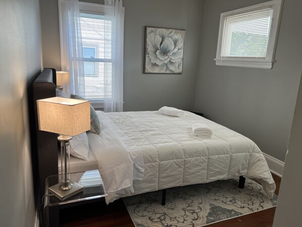 Un dormitorio ordenado con cama, lámpara de noche y una obra de arte floral enmarcada en la pared.