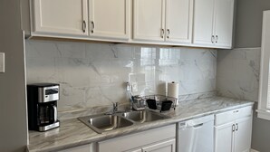 A kitchen with white cabinets, a marble backsplash, a coffee maker, a sink, and a dishwasher. - Spacious 2 bed room apartment near Shaker, Cleveland clinic, CWRU, Van aken.  (Cleveland Heights)