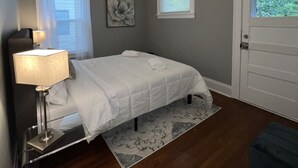 A bedroom with a bed, a ceiling fan, a window with blinds, a door, and a nightstand with a lamp. - Spacious 2 bed room apartment near Shaker, Cleveland clinic, CWRU, Van aken.  (Cleveland Heights)