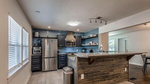 Een moderne keuken met een centraal eiland, roestvrijstalen apparatuur en blauwe spatborden.