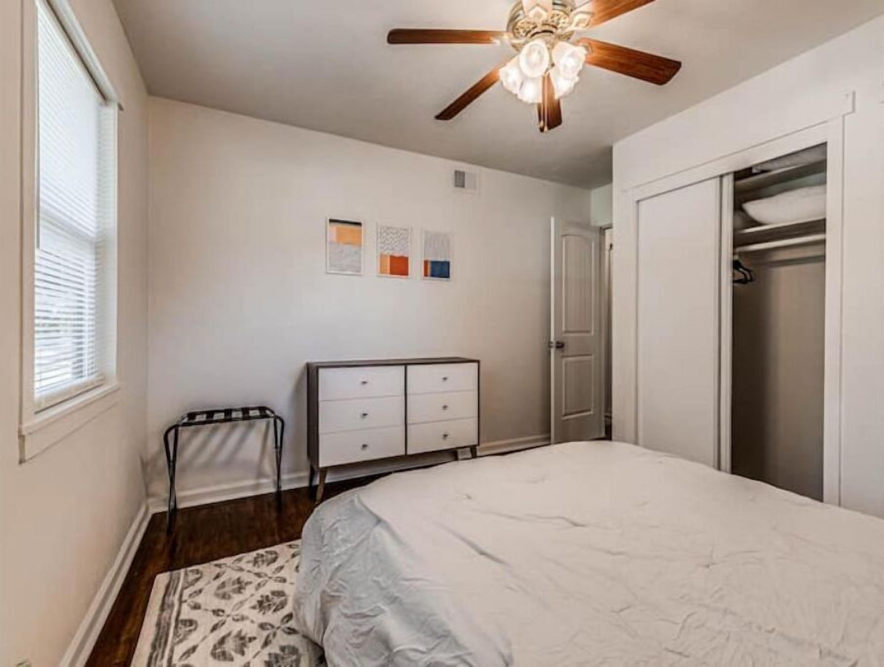 A bedroom with a bed, a dresser, a closet, and a ceiling fan.