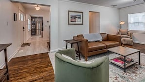 Een moderne woonkamer met een bruine leren bank, een groene fauteuil en een salontafel. In de achtergrond bevindt zich een keuken met roestvrijstalen apparatuur.