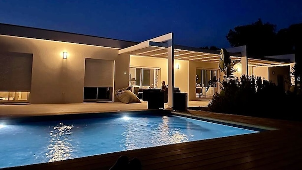 Ein modernes Haus mit Swimmingpool, einer überdachten Terrasse und einem hellen Innenraum.