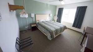 A hotel room with a bed, a desk, a chair, a ceiling fan, a window with curtains, and a wall-mounted lamp. - Rewak Studios: Gigabit Powered WiFi! Hotel-Style Furnished Studios--Easy Walk to Lots of Places (Fairbanks)