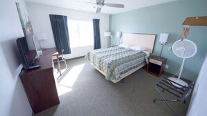 A hotel room with a bed, a desk, a chair, a desk lamp, a standing fan, and a ceiling fan. - Rewak Studios: Gigabit Powered WiFi! Hotel-Style Furnished Studios--Easy Walk to Lots of Places (Fairbanks)