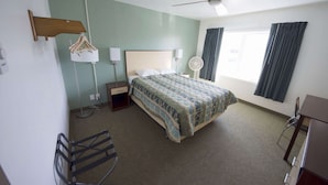 Habitación de hotel con cama, escritorio, silla, ventilador de techo, ventana con cortinas y una lámpara de pared.