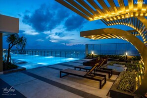 Ein moderner Poolbereich im Freien mit Liegestühlen und Blick auf das Meer im Dämmerlicht.