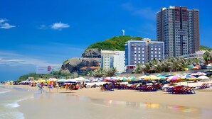 A beach with colorful umbrellas, a rocky hill, and modern buildings in the background. - The Song Vung Tau Apartment Cookies (Ho Chi Minh City)