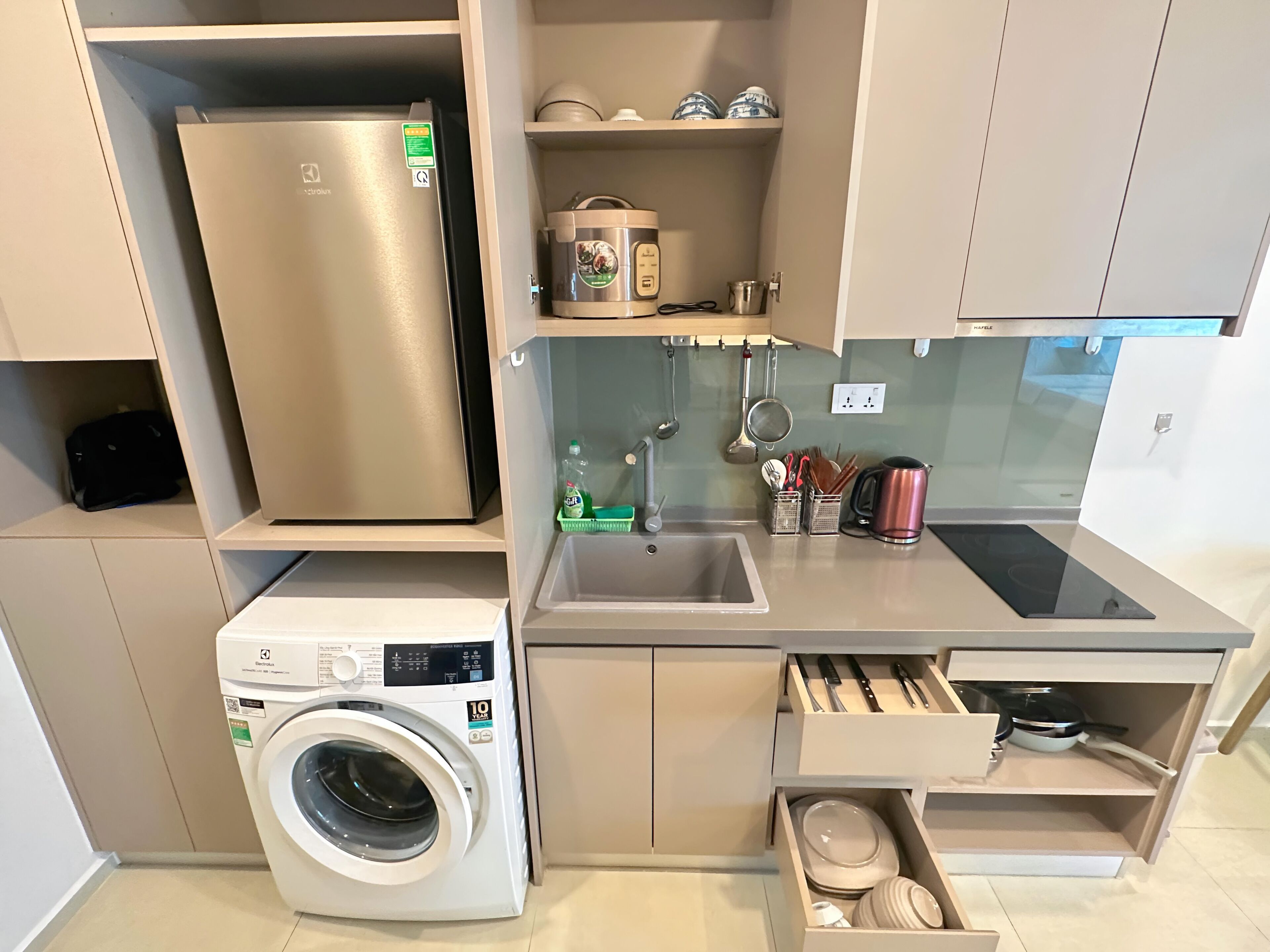 A compact kitchen with a stainless steel refrigerator, a built-in washing machine, a sink, and a stove.