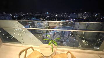 A balcony with a glass railing, two wooden chairs, a small table, and a potted plant.