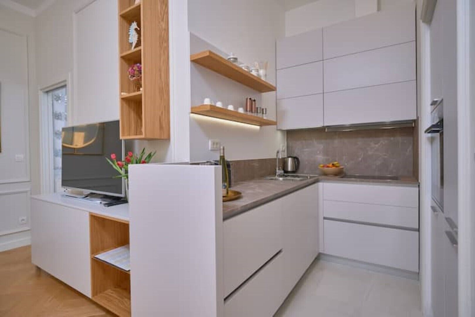 A modern kitchen with white cabinetry, a built-in island, and a flat-screen TV.