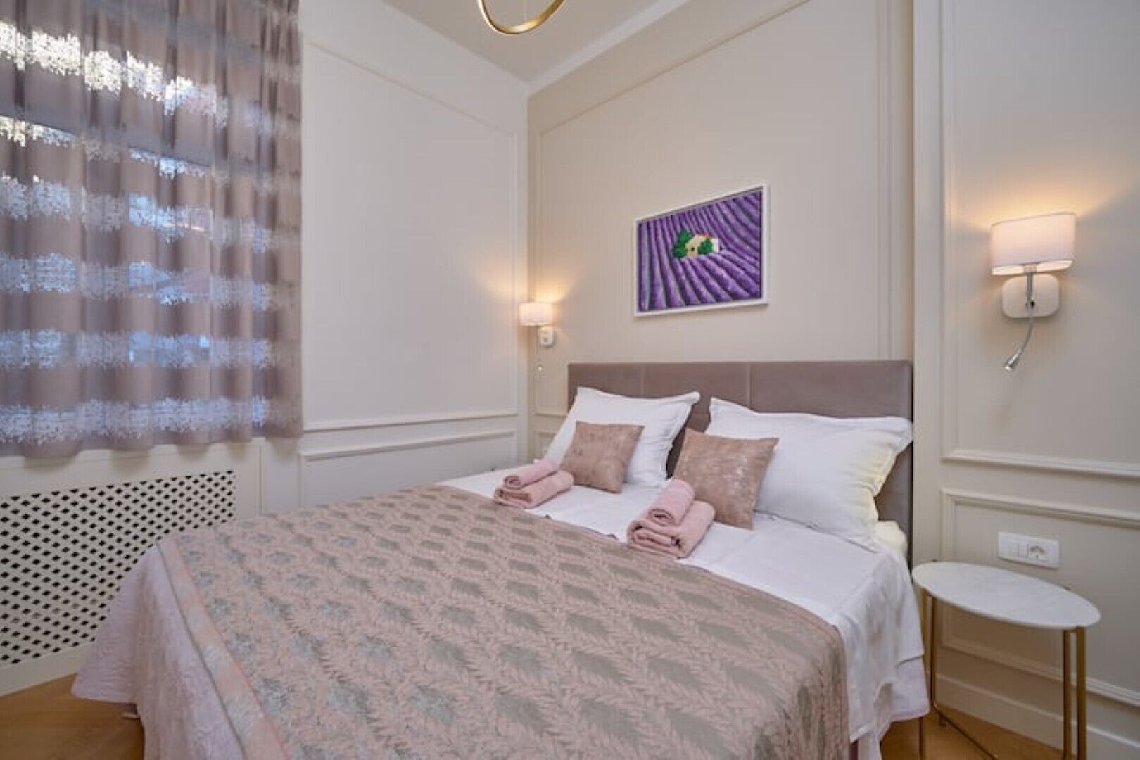 A neatly made bed with pink towels, a headboard, and a wall-mounted picture.