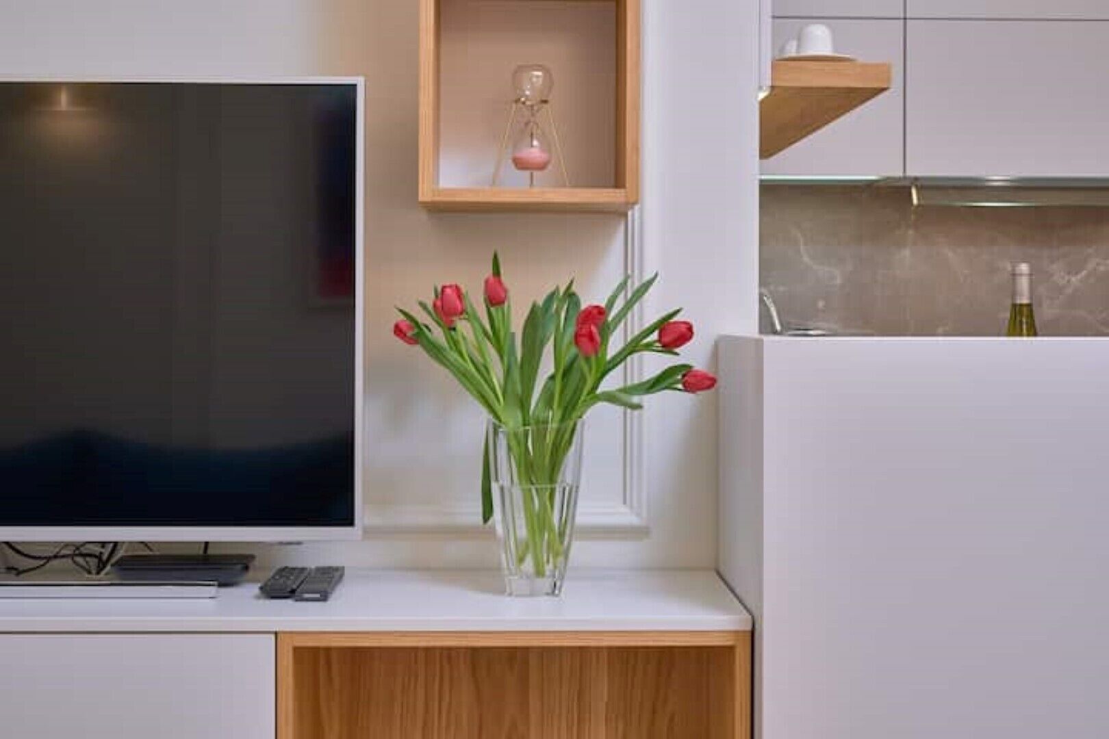 Una cocina moderna con televisor, un armario de madera y un jarrón con tulipanes rojos.