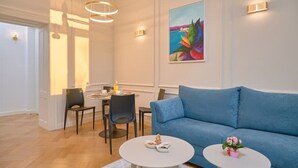 A modern living room with a blue sofa, two white coffee tables, and a dining area with chairs and a table. - Salve Luxury Apartment by Litto (Split)