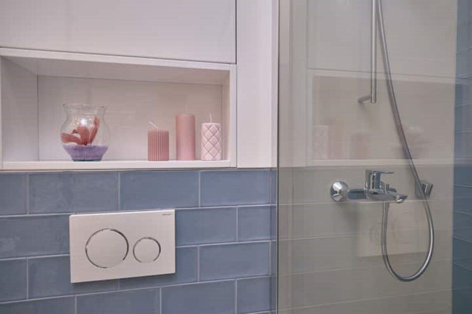 A bathroom with a shower, a shelf with decorative items, and a thermostat.