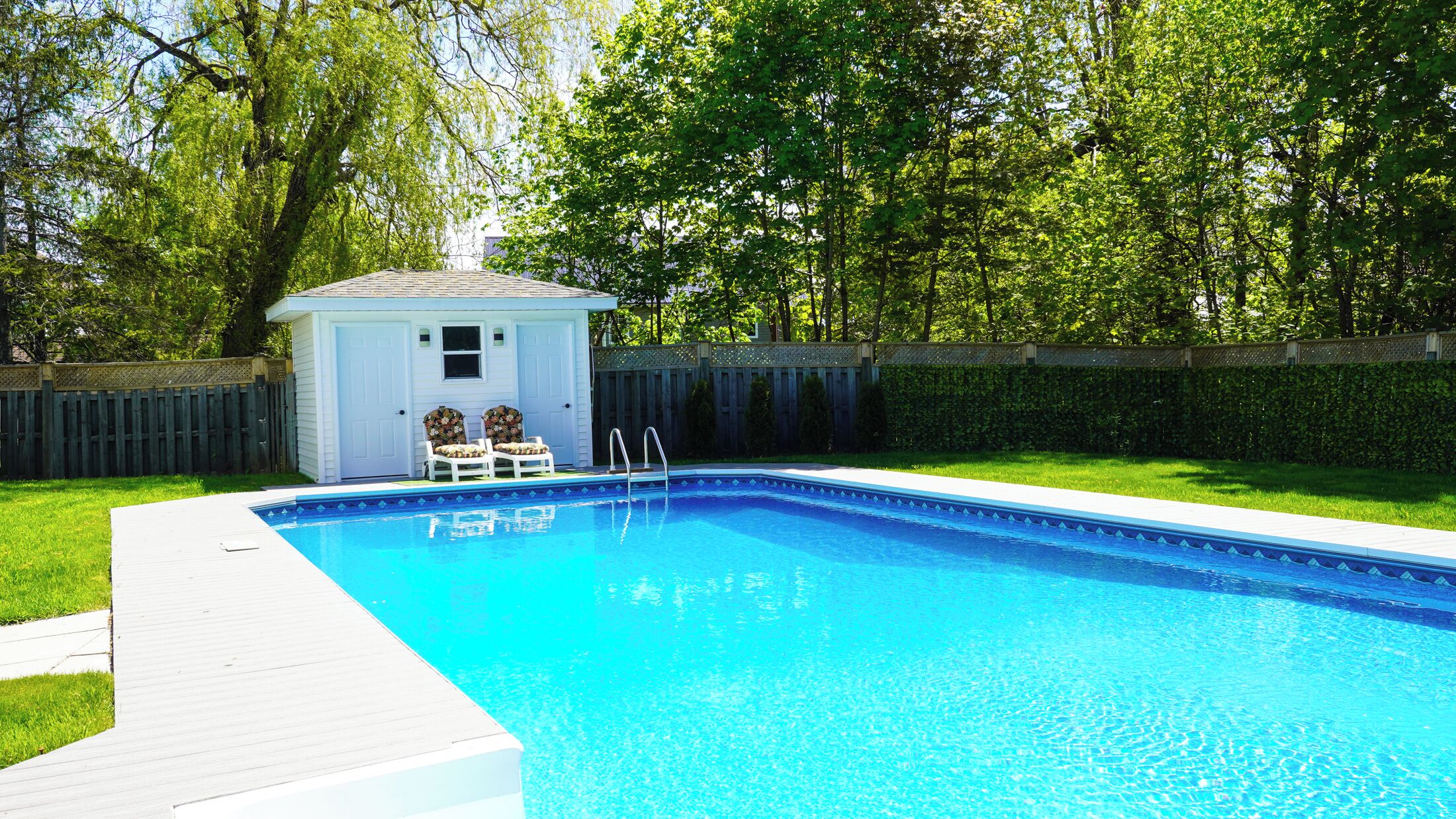 A rectangular swimming pool with a wooden deck and two chairs.