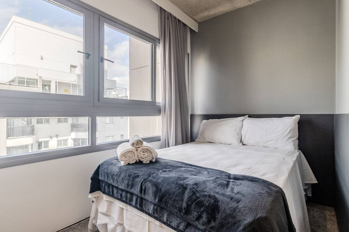 A hotel room with a bed, a window, and a view of buildings outside.