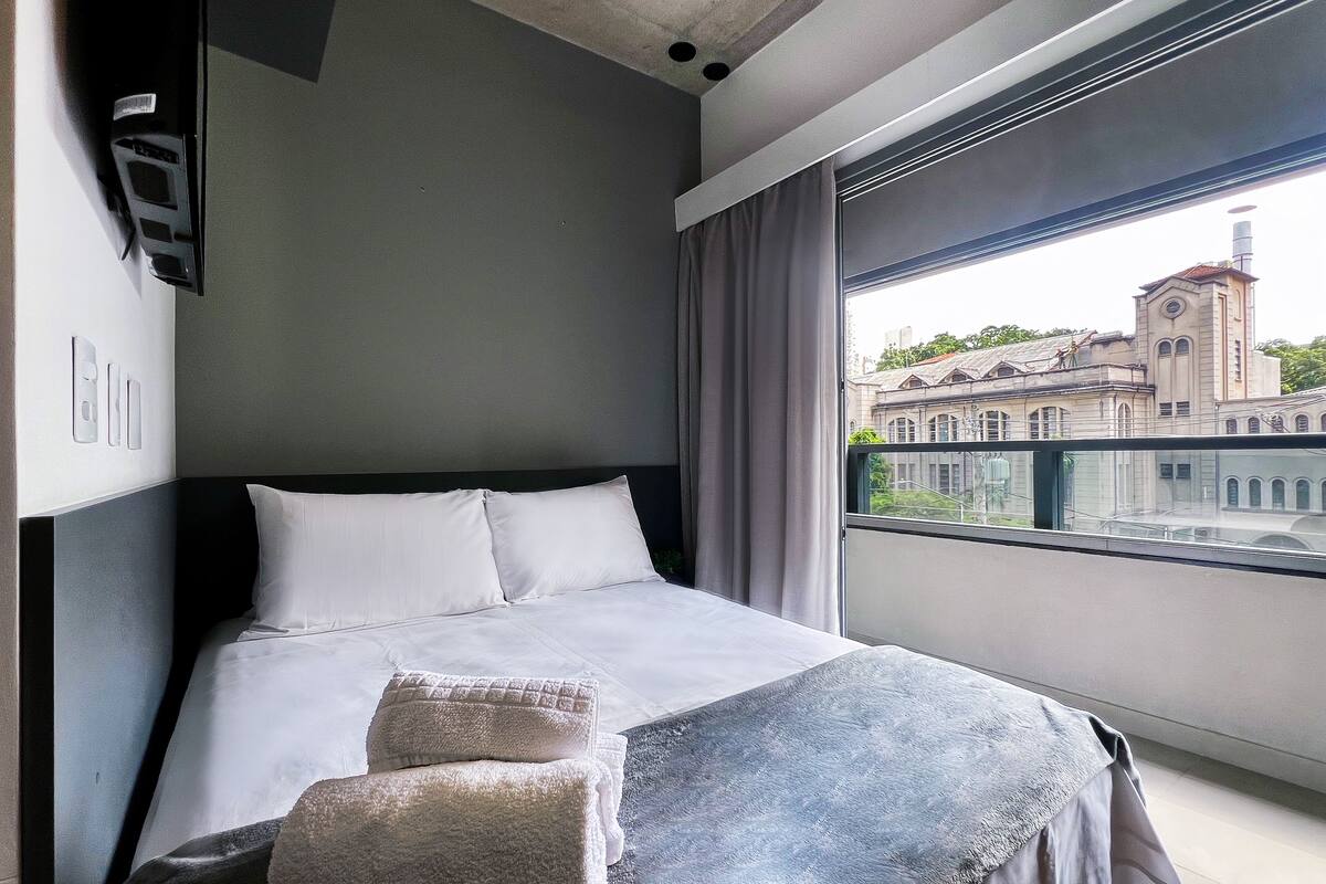 A modern hotel room with a large bed, a view of a historic building, and a window with curtains.