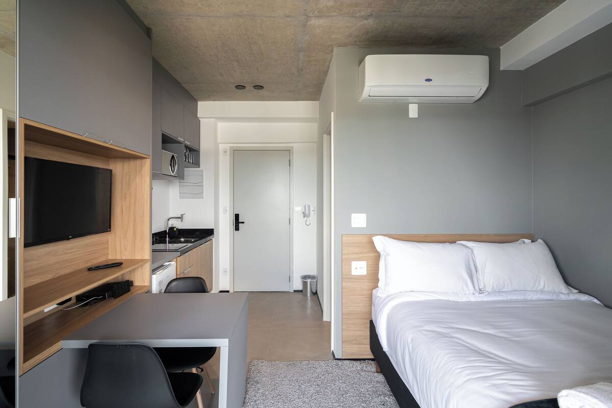 A modern hotel room with a bed, a TV, a desk, and a kitchenette.