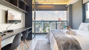 A modern hotel room with a large bed, a desk with a TV, and a city view through large windows. - 360 VN On Lorena (São Paulo)