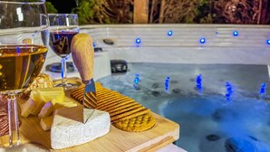 En træplade med ost, kiks og vinglas på et bord nær en jacuzzi med blå lys.