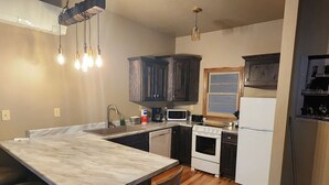 A kitchen with a marble countertop, wooden cabinets, a microwave, stove, and a refrigerator. - Nugget Suite - Main Street (Deadwood)