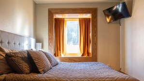 A bedroom with a large bed, a window with curtains, and a floor lamp. - Nugget Suite - Main Street (Deadwood)