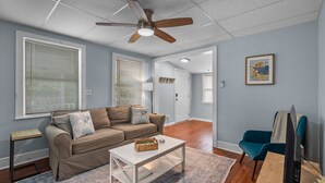 A living room with a brown sofa, a white coffee table, a blue armchair, and a ceiling fan. - The Teal Door is a 3 Bedroom 1 Bath Unit. Sleeps 6. Linens Included! (Carolina Beach)
