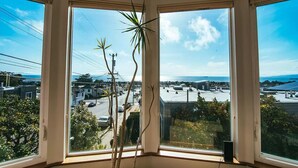 Ein Zimmer mit drei großen Fenstern und Blick auf eine Küstenstadt, einschließlich Gebäude und einer Straße.