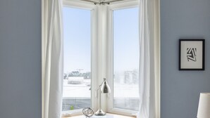 Ein Schlafzimmer mit großem Fenster, Schreibtisch mit Lampe und Bett mit Decke.
