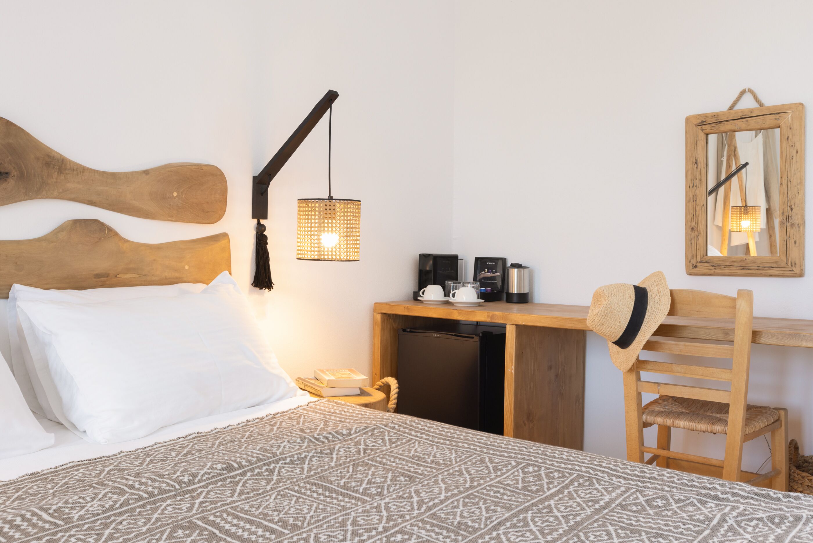 Une chambre d’hôtel bien rangée, avec un lit, un petit bureau, une chaise, un luminaire suspendu et un miroir au mur.