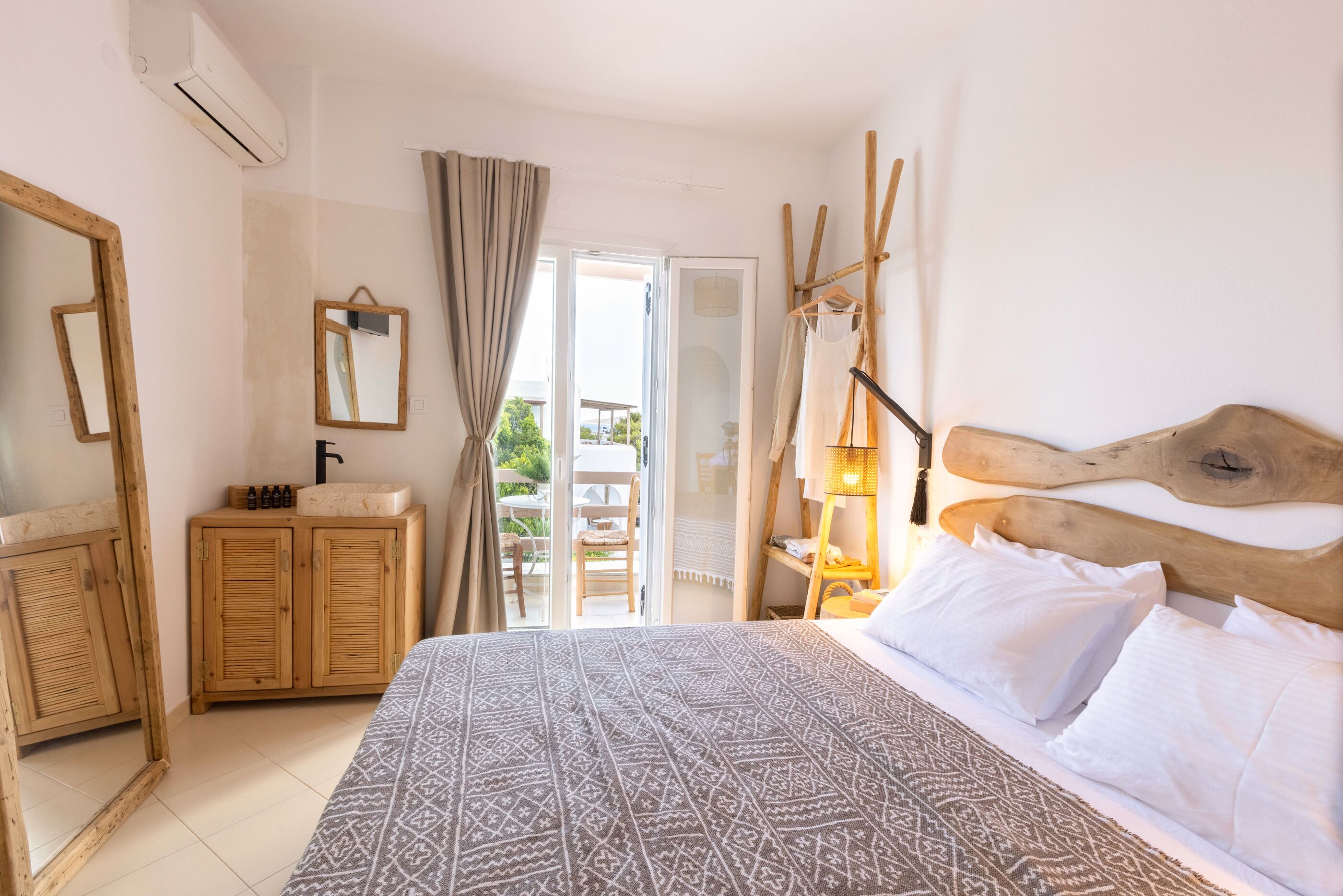 Un dormitorio con cama, cabecera de madera, cómoda de madera, un espejo y una ventana con cortinas.